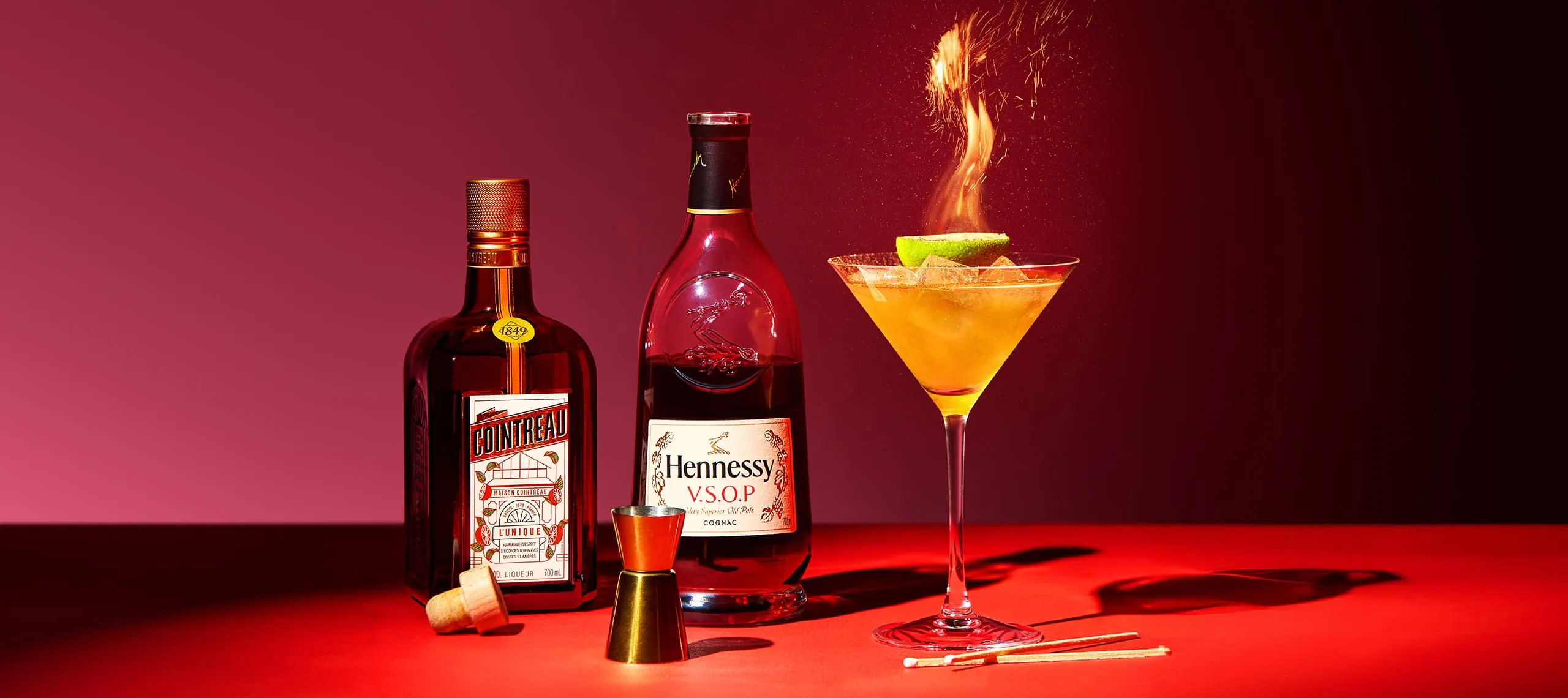 Hennessy V.S.O.P and Cointreau bottles along side Flaming cocktail in a martini glass with lime garnish